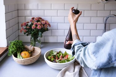 Cropped image of woman seasoning salad at kitchen counter