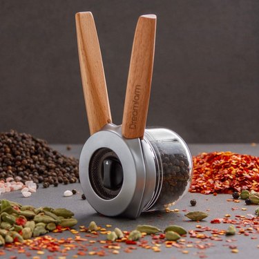Dreamfarm pepper grinder on a grey countertop, surrounded by whole spices