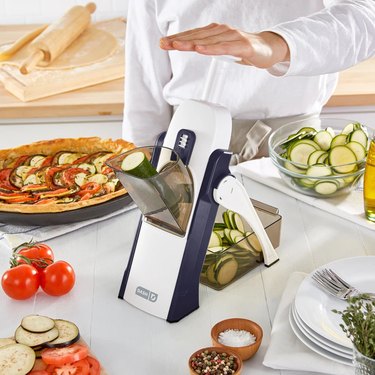 Dash mandoline slicer on a countertop surrounded by food