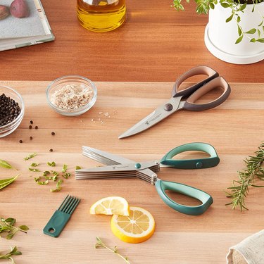 Two pairs of Henckels kitchen shears with herbs and lemons, on a butcher-block countertop