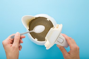 Young adult woman hand holding spoon with white powder of citric acid for descaling kettle