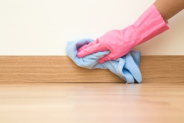 Hand in rubber protective glove with microfiber cloth wiping a baseboard