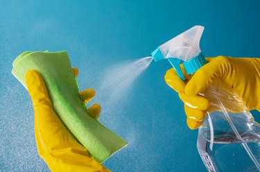 Gloved hands spray liquid on cleaning cloth