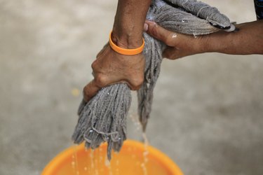Cropped Hand Squeezing Mop Over Orange Bucket