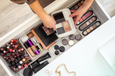 Woman hands neatly organising makeup and cosmetics in the drawer of vanity dressing table
