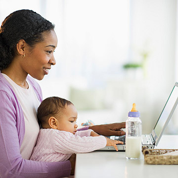 woman holding baby typing on computer